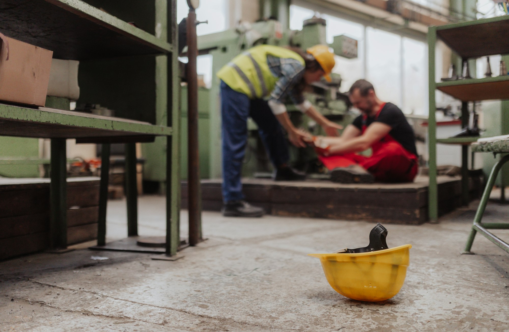 Woman is helping her colleague after accident in factory. First aid support on workplace concept.
